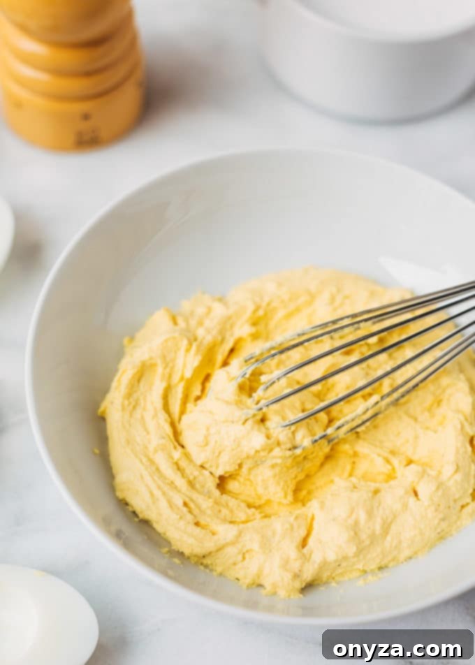 deviled egg filling in a white bowl with a whisk