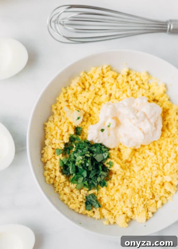 Rustic Italian Deviled Eggs with Garlic and Basil 3 Close-up of crumbled egg yolks being mixed with chopped fresh basil, creamy mayonnaise, and minced garlic in a bowl
