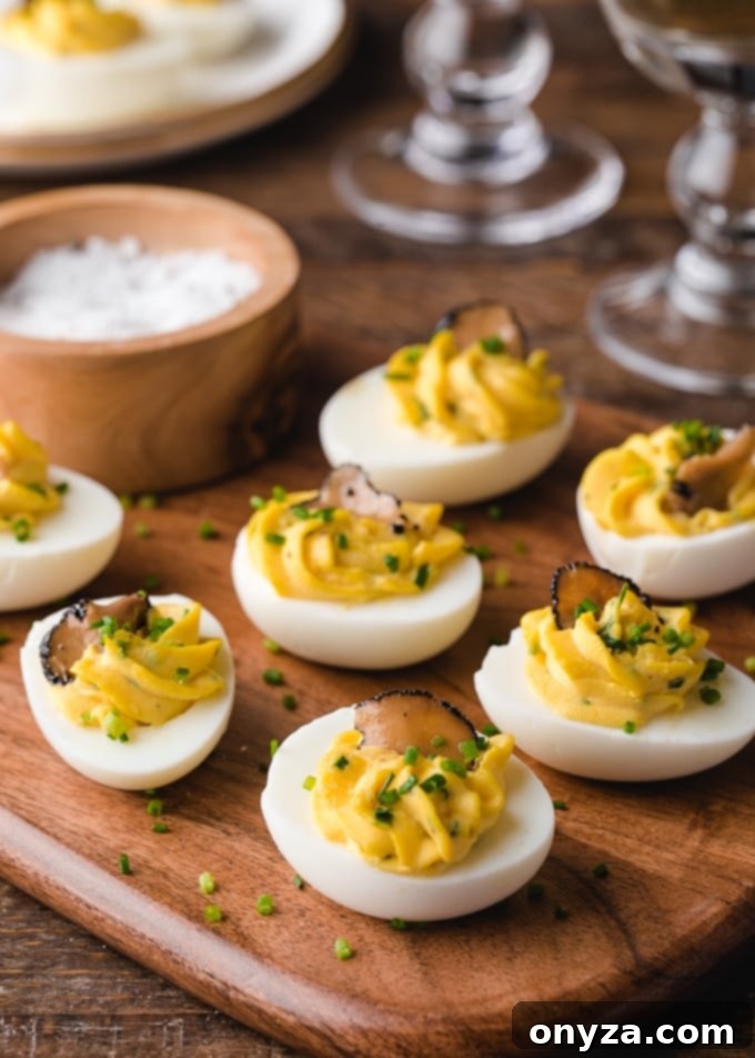 Truffled deviled eggs garnished with chives on a rustic wooden board, ready to be served as an elegant appetizer.