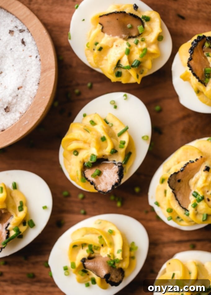 Overhead view of a platter of truffled deviled eggs, garnished with fresh chives and delicate shavings of black truffles, ready for a gourmet spread.