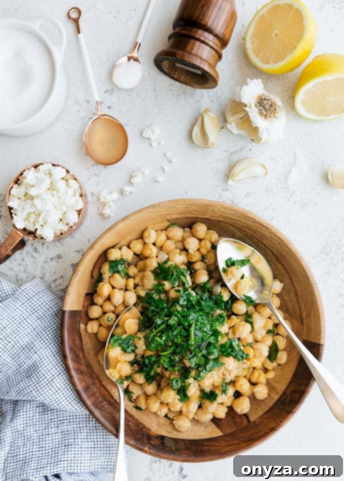 Mediterranean Chickpea & Feta Salad 3 An overhead photo capturing the process of mixing garbanzo bean salad ingredients in a wooden bowl, highlighting the fresh textures.