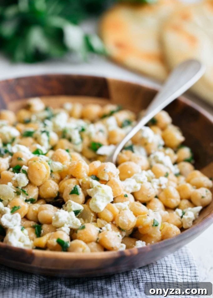 Mediterranean Chickpea & Feta Salad 5 A close-up shot of chickpea salad with feta in a wooden bowl, ready to be served with a spoon.