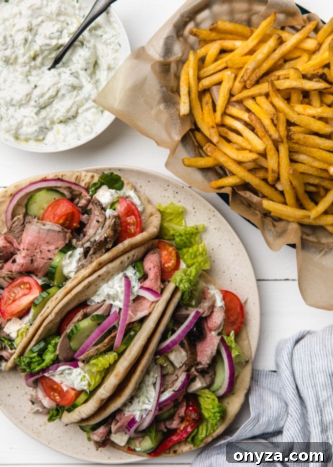 A perfectly assembled plate featuring loaded lamb pitas, accompanied by a side of golden French fries and a small bowl of creamy tzatziki for dipping.