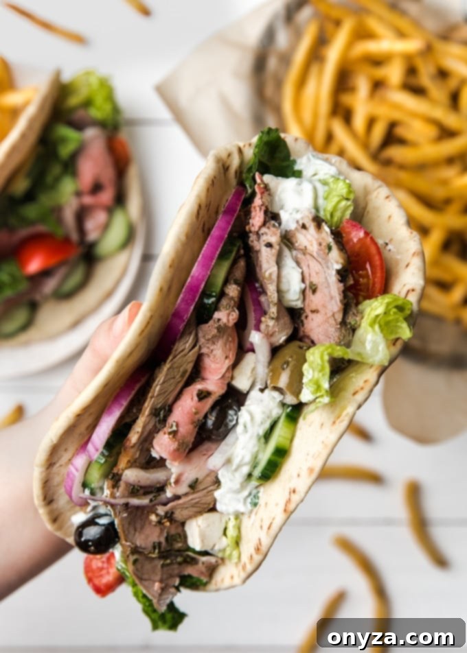 A close-up shot of a hand holding a perfectly assembled roasted lamb pita, overflowing with succulent meat and fresh Mediterranean fillings.