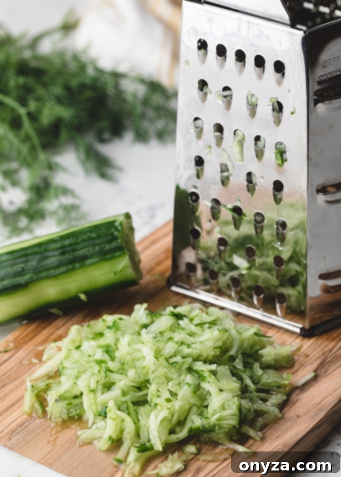 Creamy Homemade Tzatziki 2 Close-up of shredded cucumber on a cutting board next to a box grater, illustrating the preparation step.