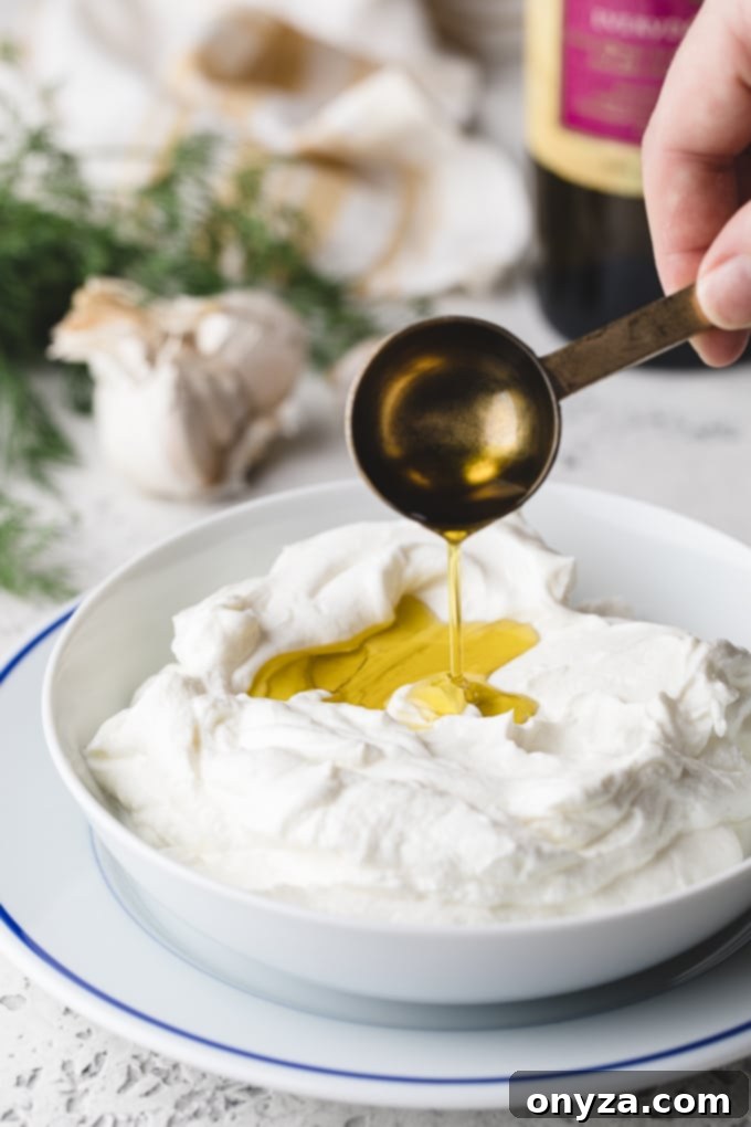 Creamy Homemade Tzatziki 3 Olive oil being slowly drizzled into a bowl of thick Greek yogurt, a key step in making creamy Tzatziki.