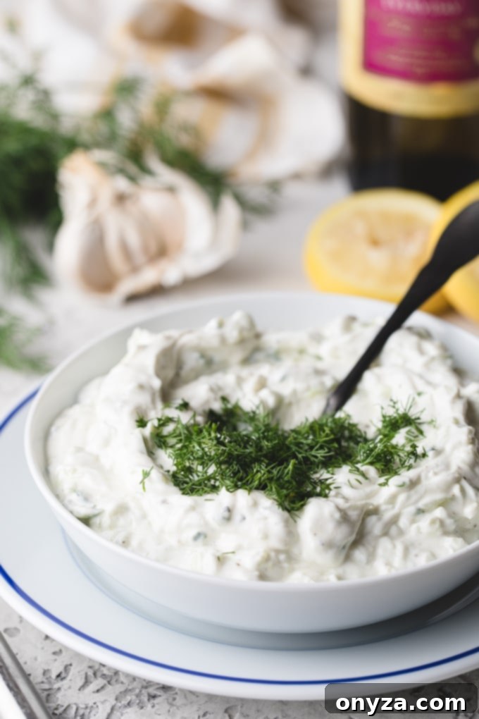 Creamy Homemade Tzatziki 4 Freshly chopped dill being added to a bowl of creamy Tzatziki sauce with a spoon, ready for mixing.