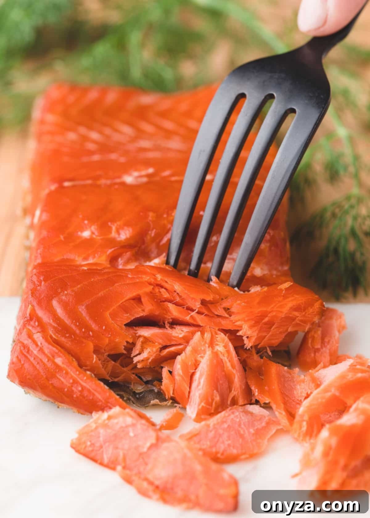 fillet of hot smoked salmon on a wood and marble board being flaked with a fork