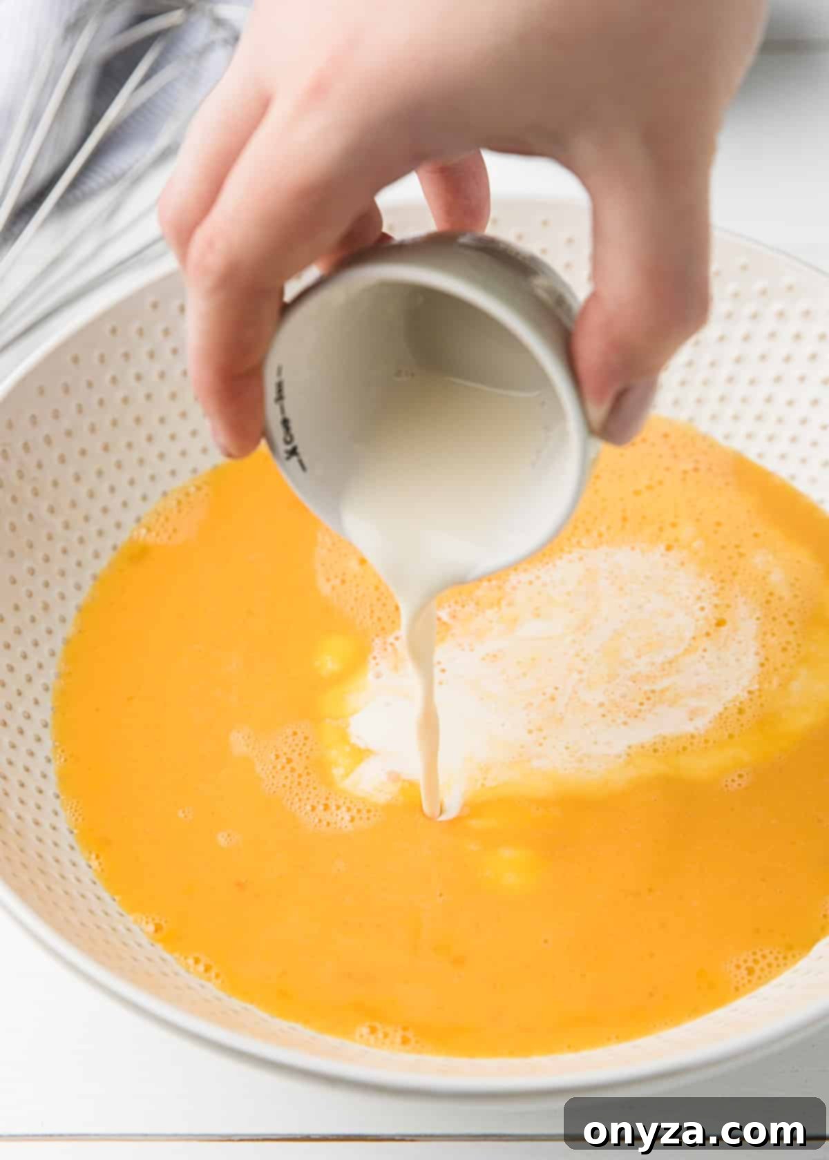 pouring heavy cream into a white ceramic bowl of beaten eggs