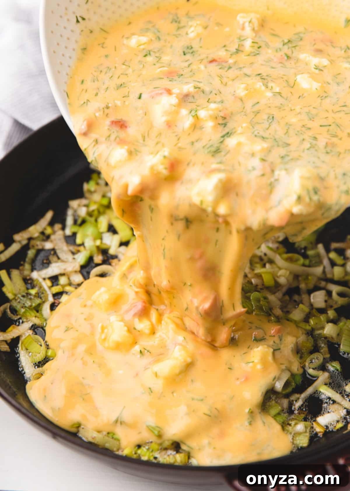 frittata egg mixture being poured over sauteed leeks in a frying pan