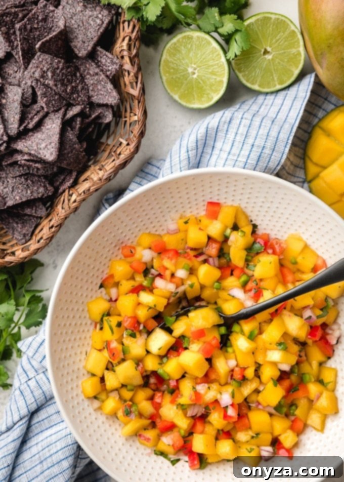 A bowl of vibrant mango salsa, freshly prepared and ready to serve, next to a basket of crispy blue corn chips.