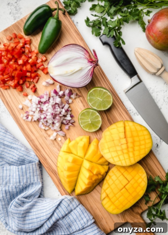 Freshly chopped red bell pepper, red onion, and perfectly scored mango halves arranged on a rustic wooden cutting board, ready for the salsa.