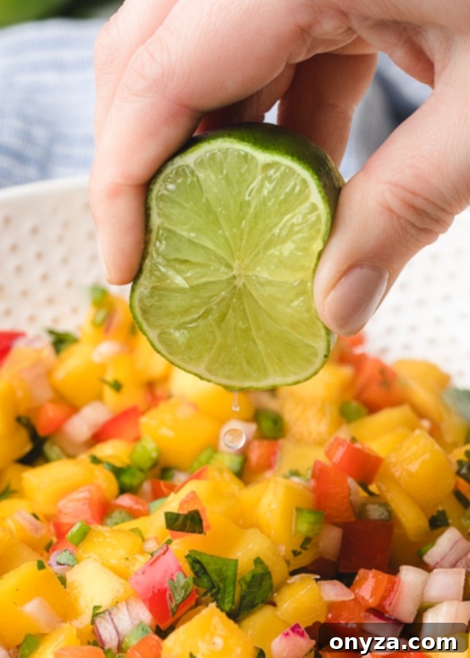 Freshly squeezed lime juice being added to a mixing bowl filled with colorful mango salsa ingredients, enhancing its zesty flavor.