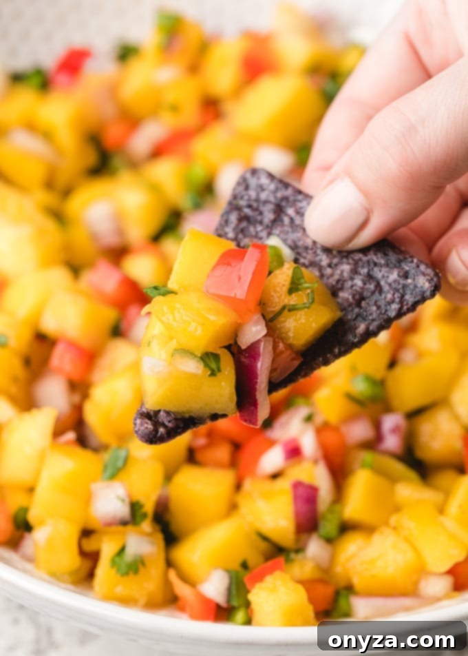 A close-up shot of vibrant mango salsa delicately scooped onto a blue corn chip, highlighting its fresh ingredients and inviting texture.