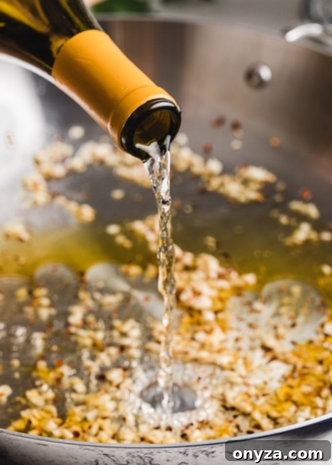 A close-up shot of white wine being poured into a pan filled with sautéed garlic.