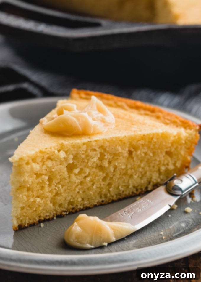 A single, inviting slice of sour cream cornbread, artfully presented on a plate with a luscious dollop of maple butter melting on top.