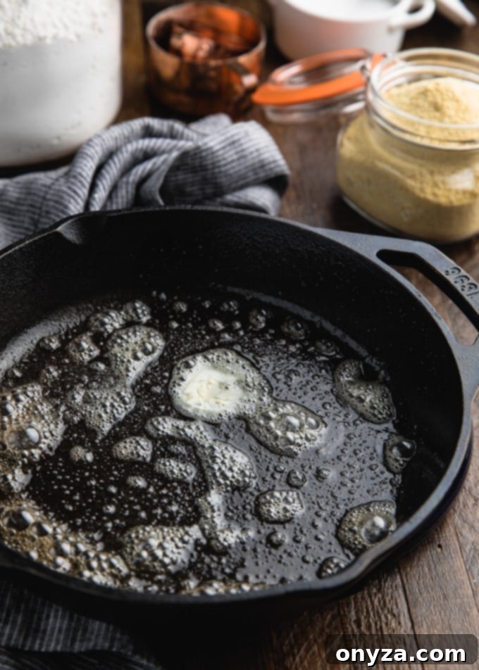 A close-up shot of butter gently melting and bubbling in a perfectly heated cast iron skillet, preparing for cornbread batter.