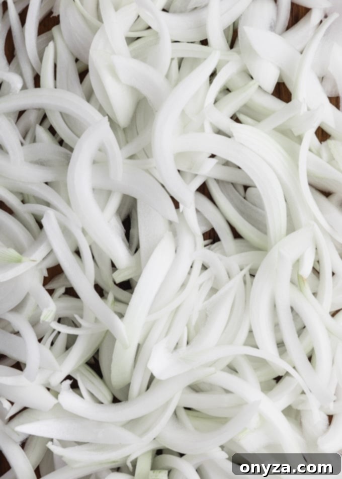 Mükemmel Karamelize Soğan Yapımı 3 A close-up view of a neatly piled mound of thinly sliced yellow onions, ready for caramelization.