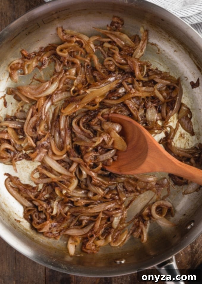 Mükemmel Karamelize Soğan Yapımı 5 An overhead close-up shot of perfectly caramelized onions glistening in a pan with a wooden spoon, showcasing their rich, golden-brown hue.