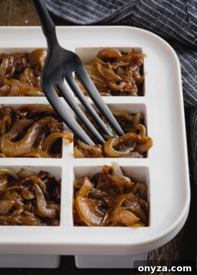 Mükemmel Karamelize Soğan Yapımı 6 A fork carefully placing a portion of golden caramelized onions into a white silicone ice cube tray, illustrating the process of preparing them for freezer storage.