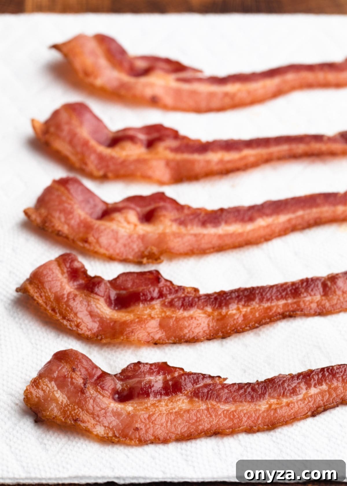 Crispy baked bacon strips arranged neatly on a bed of paper towels to drain excess fat, ready for serving.