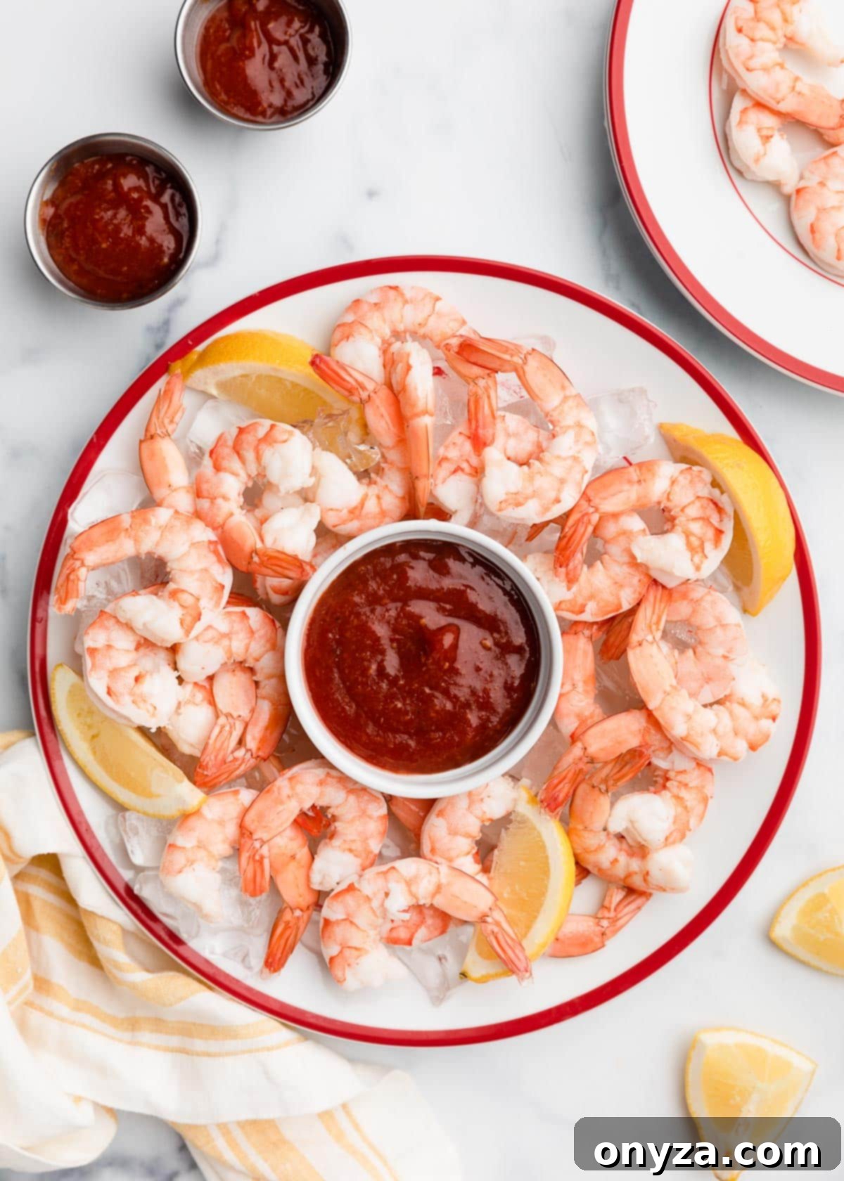 overhead of shrimp cocktail on a red-rimmed white platter with cocktail sauce and lemon wedges
