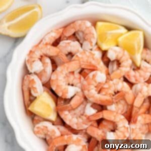 overhead of poached shrimp in a white fluted pie plate on a marble board with lemon wedges