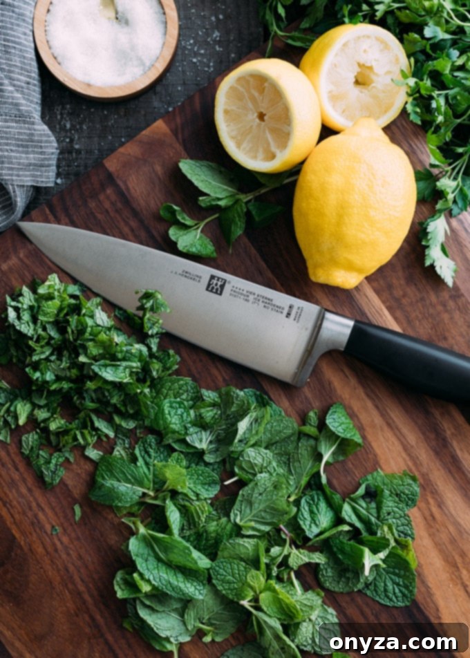 chopped mint on a wood cutting board with a chef's knife and lemons