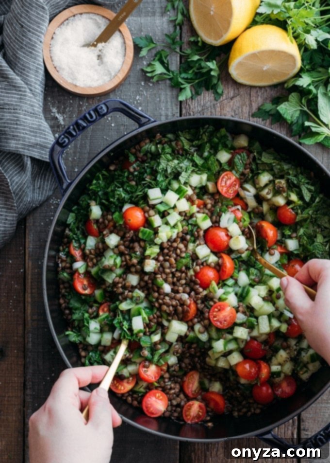 overhead photo of tossing lentil tabbouleh salad in a cast iron pan with gold colored spoons