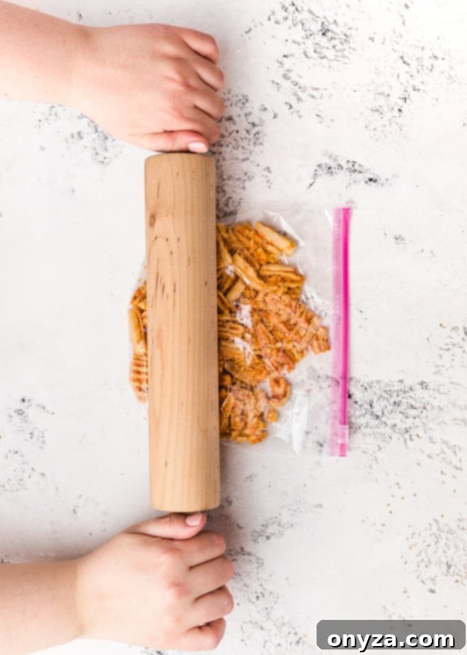 A plastic bag of cheese crisps being crushed with a rolling pin, demonstrating a simple method for preparing toppings.
