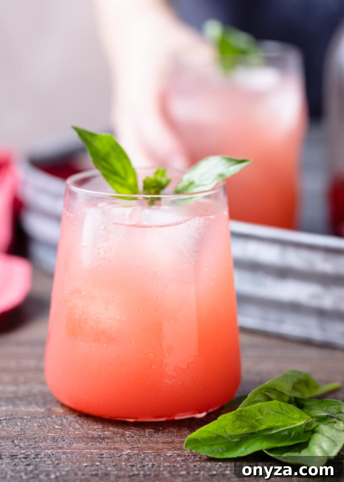 A glass of homemade strawberry basil soda, garnished with fresh basil leaves and a strawberry slice, sitting on a rustic wooden board.
