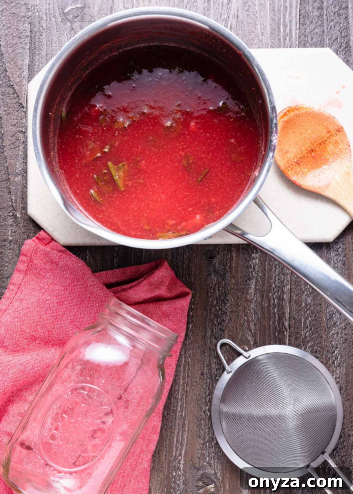 An overhead photo captures a vibrant red, simmered strawberry basil syrup resting in a saucepan, ready for cooling.