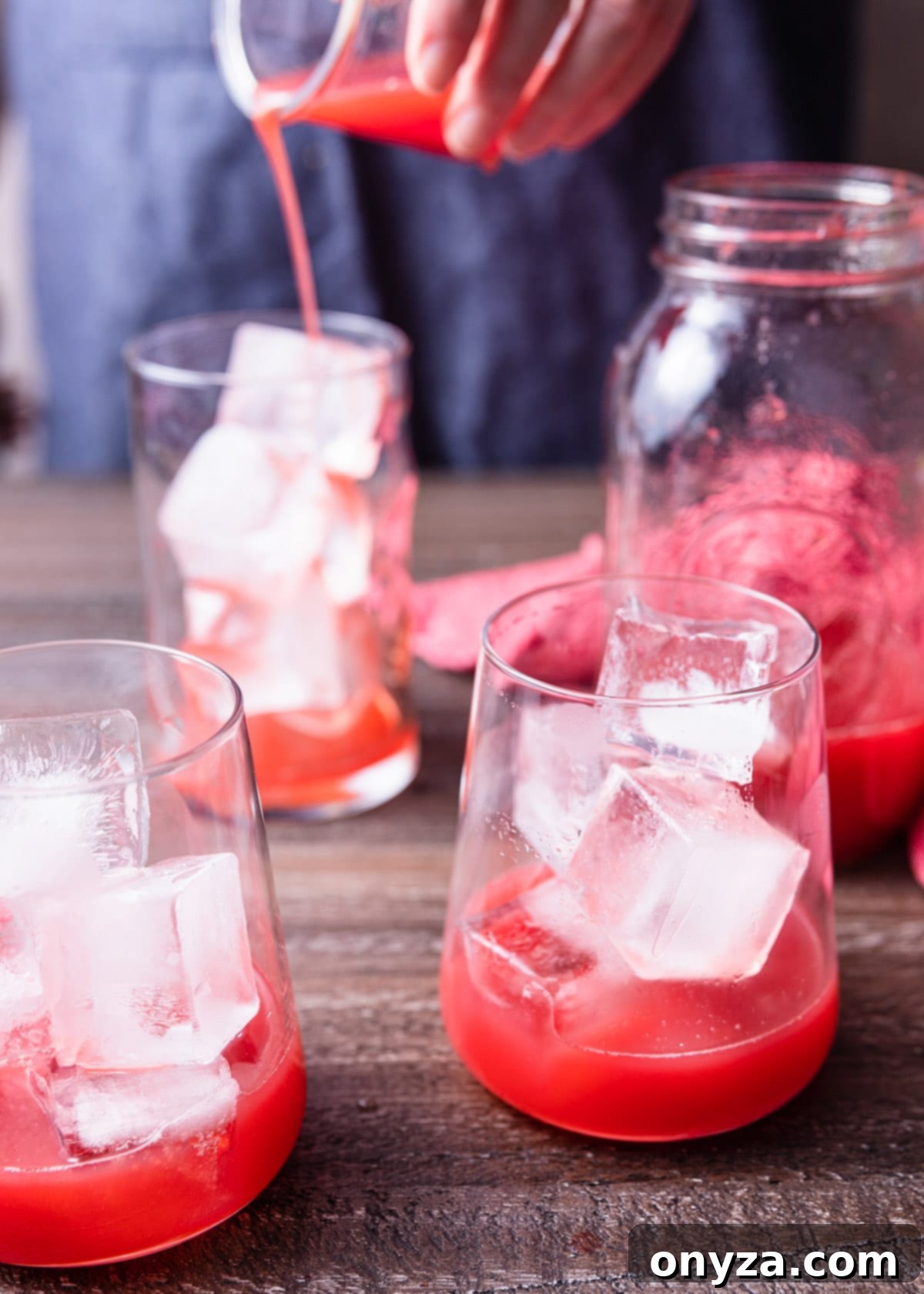Two glasses, filled with ice, have vibrant strawberry basil syrup poured into them, ready to be topped with sparkling water.