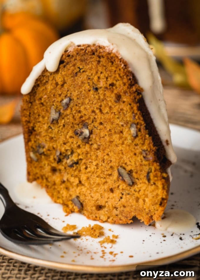 A close-up side view of a perfect slice of pumpkin pecan bundt cake on a pristine white plate, accompanied by an elegant black fork, highlighting its moist texture and delicious layers.