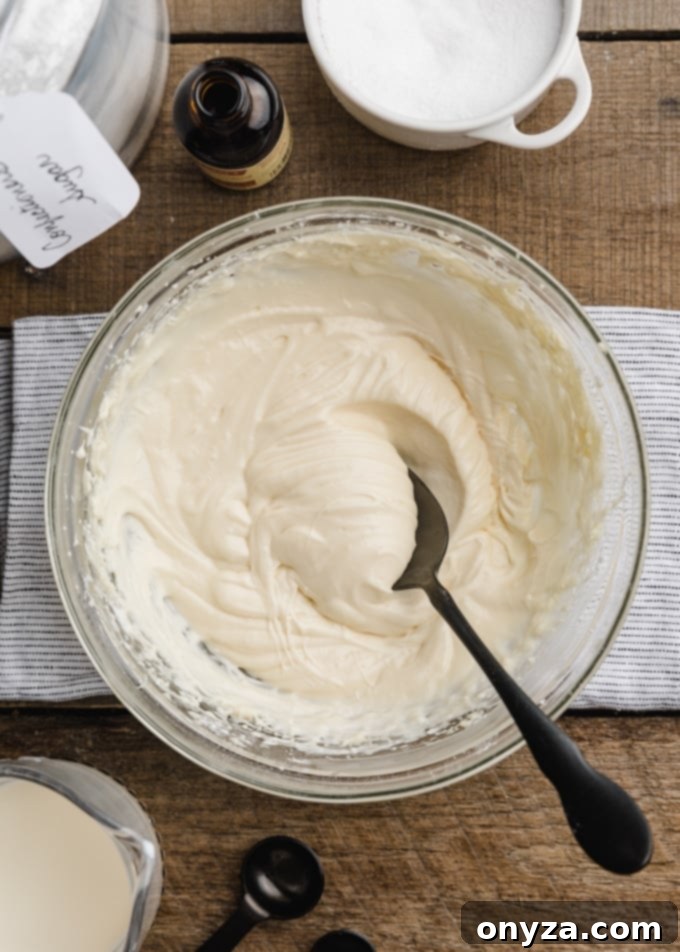 Velvety Cream Cheese Topping 5 Overhead shot of freshly made cream cheese glaze in a white bowl, with a black spoon resting in it, ready for use.