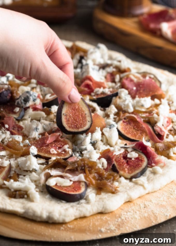 placing a sliced fresh fig onto an unbaked pizza