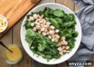 Cubed chicken breast arranged in a line in a bowl with baby spinach and romaine leaves, ready for other ingredients.