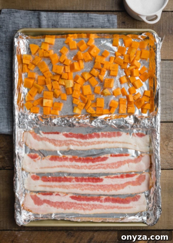 Cubed butternut squash and strips of bacon arranged on a foil-lined baking sheet, ready for roasting.