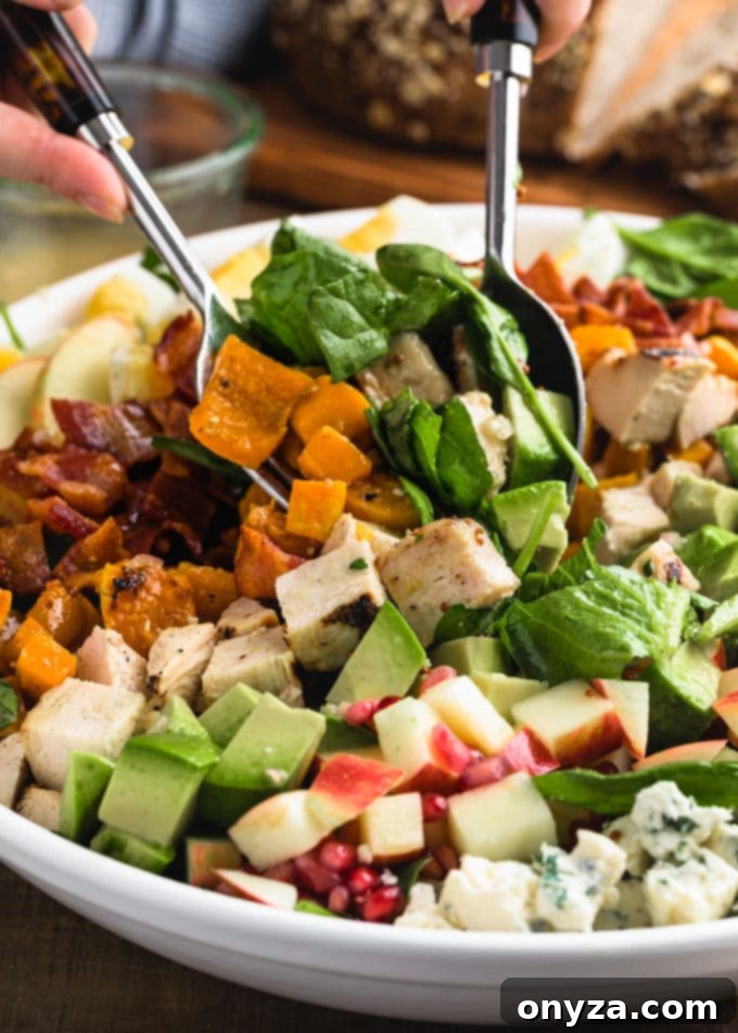 A bowl filled with various diced ingredients for a Harvest Cobb Salad, showcasing colorful cubes of chicken, apples, avocado, and blue cheese.