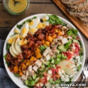 Overhead view of a beautifully arranged Harvest Cobb Salad in a white bowl, accompanied by a jar of maple-Dijon vinaigrette and slices of whole-grain bread.