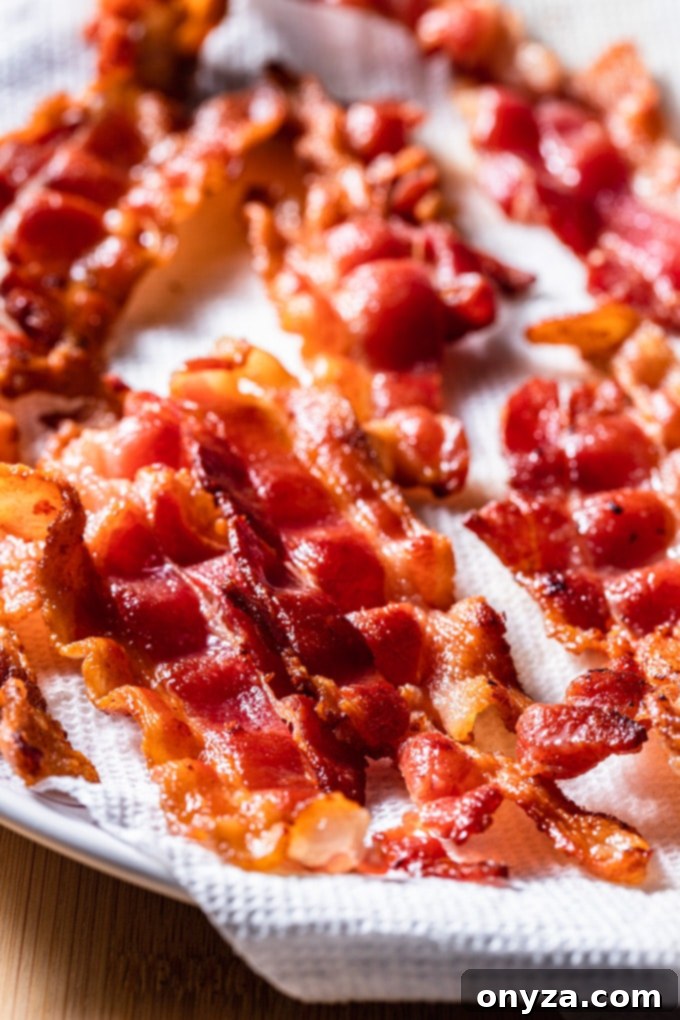 Crispy, thick-cut bacon strips cooling on a paper towel-lined plate, ready to be crumbled for a delicious loaded potato salad.
