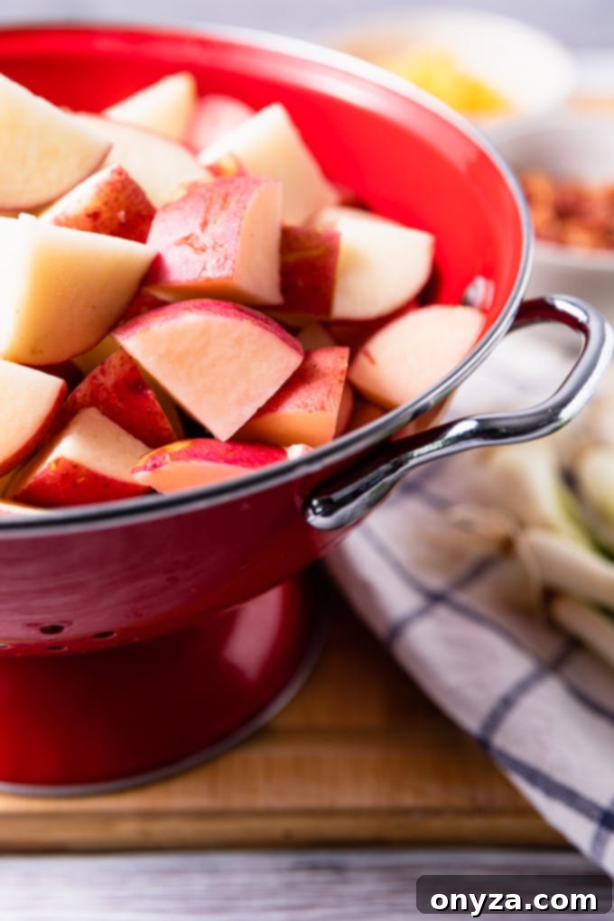 Cleaned and uniformly cubed red potatoes resting in a bright red colander, ready to be cooked for a potato salad.