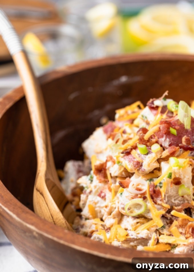 Side view of a generous serving of loaded potato salad in a rustic wooden bowl, with a wooden serving spoon, highlighting the creamy texture and delicious toppings.