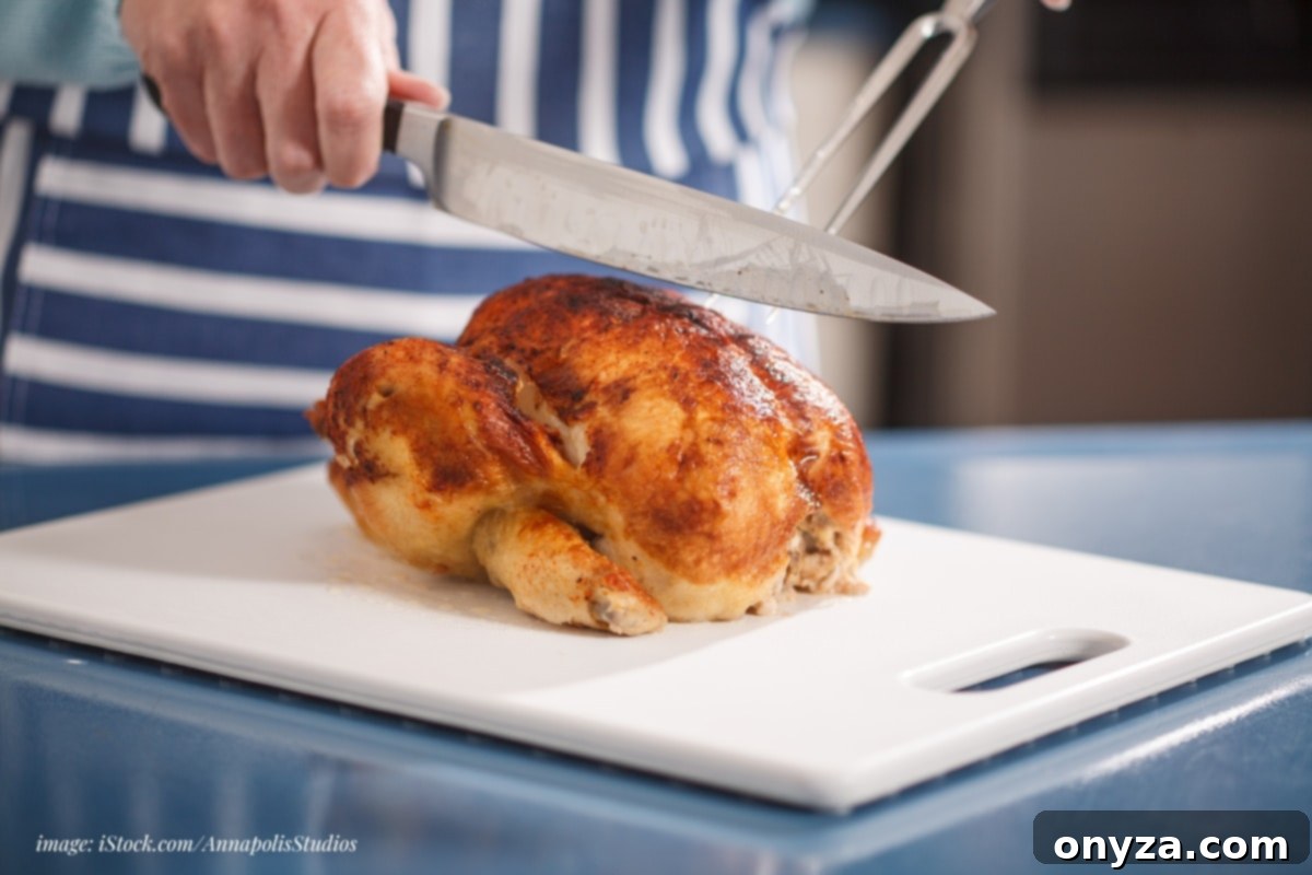 cook in a blue and white striped apron carving a rotisserie chicken on a white cutting board