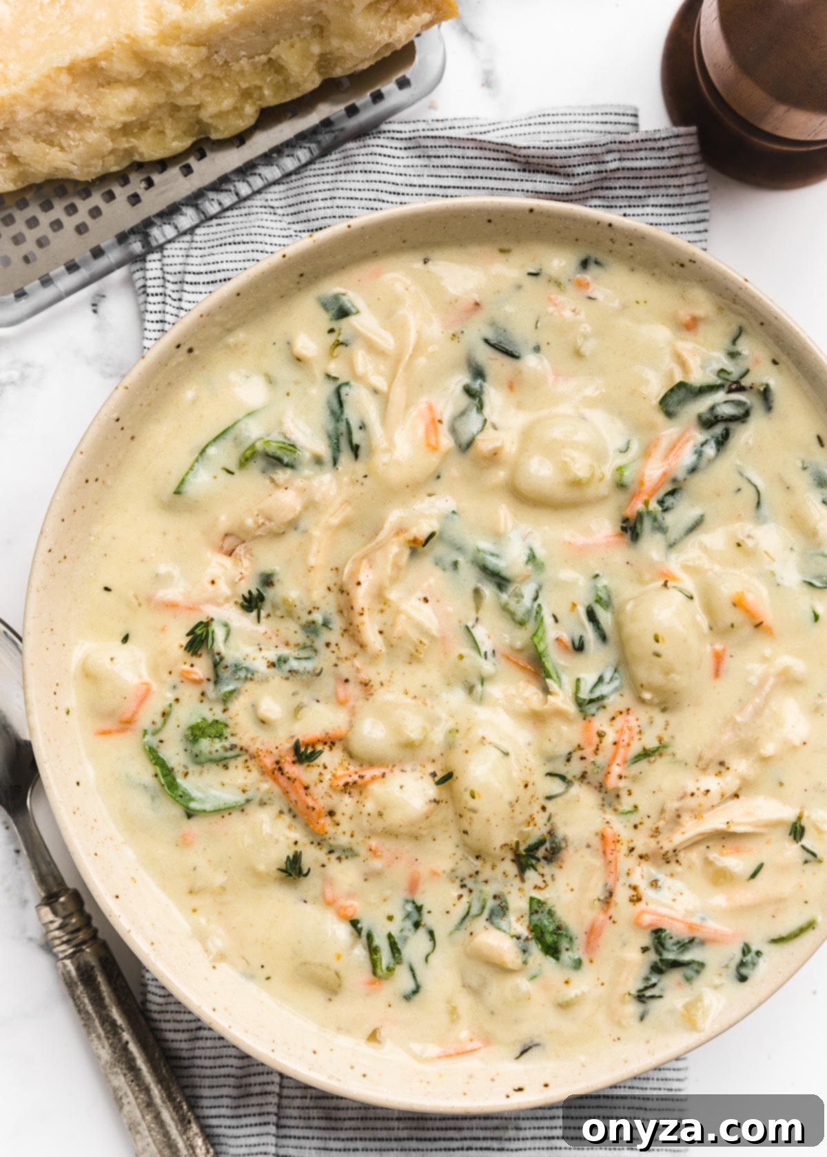 Hearty Chicken Gnocchi Comfort 2 overhead of bowl of creamy rotisserie chicken gnocchi soup on a striped napkin next to a wedge of parmesan cheese