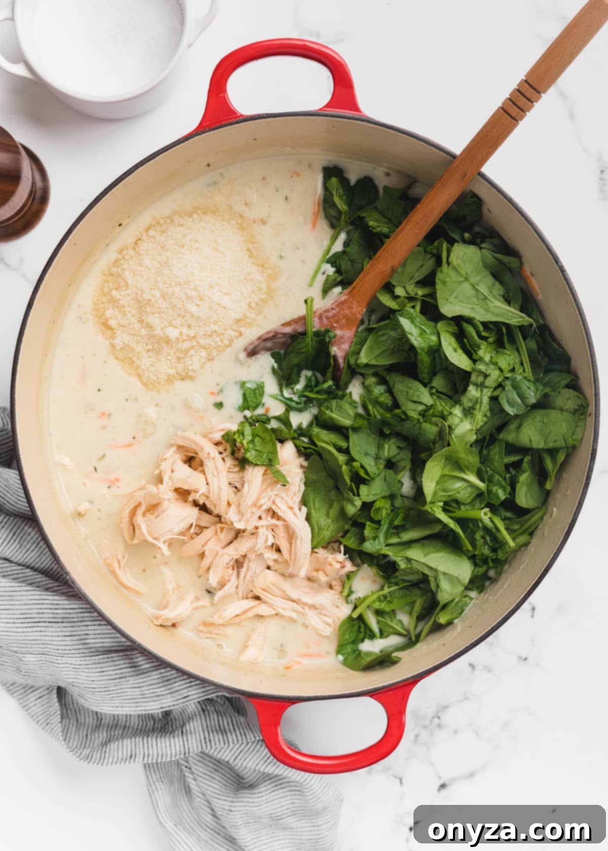 Hearty Chicken Gnocchi Comfort 11 shredded rotisserie chicken and raw baby spinach are added to a Dutch oven of soup. A wooden spoon rests in the pot.