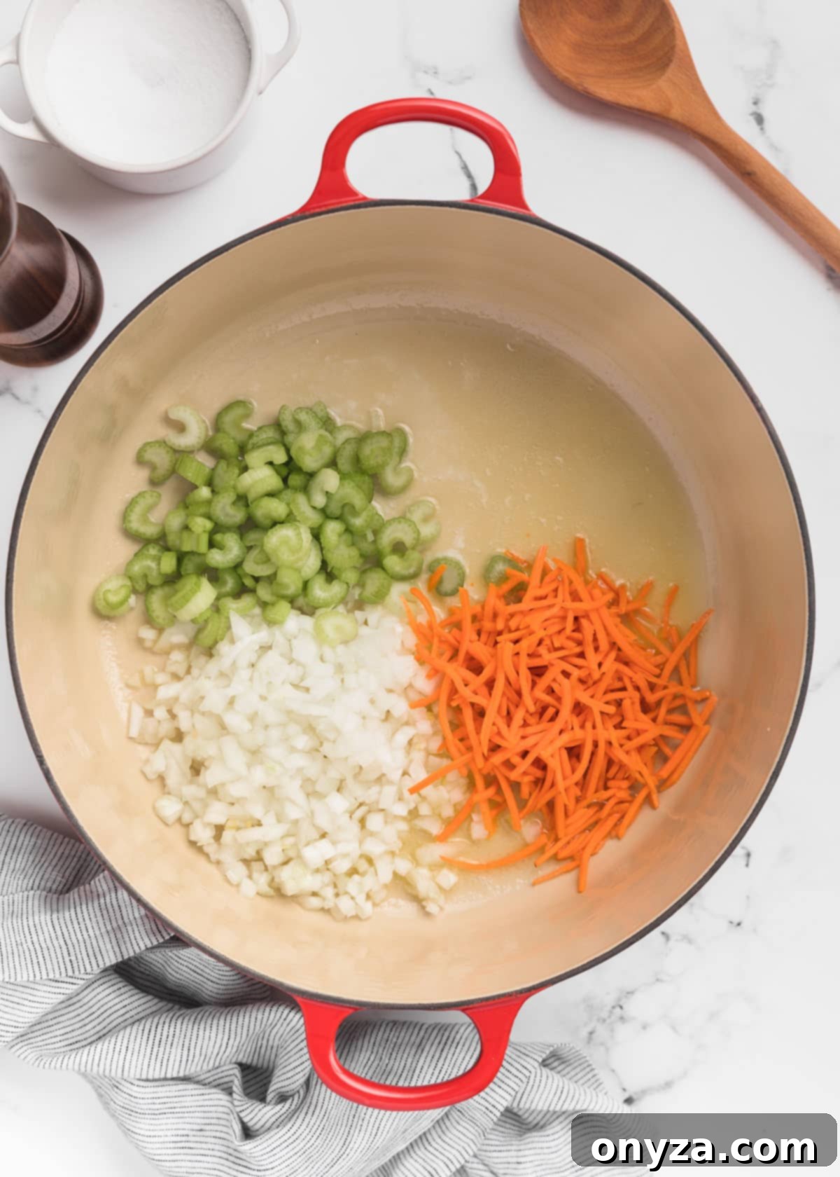 Hearty Chicken Gnocchi Comfort 4 raw carrots, celery, and onions in a Dutch oven on a white marble board