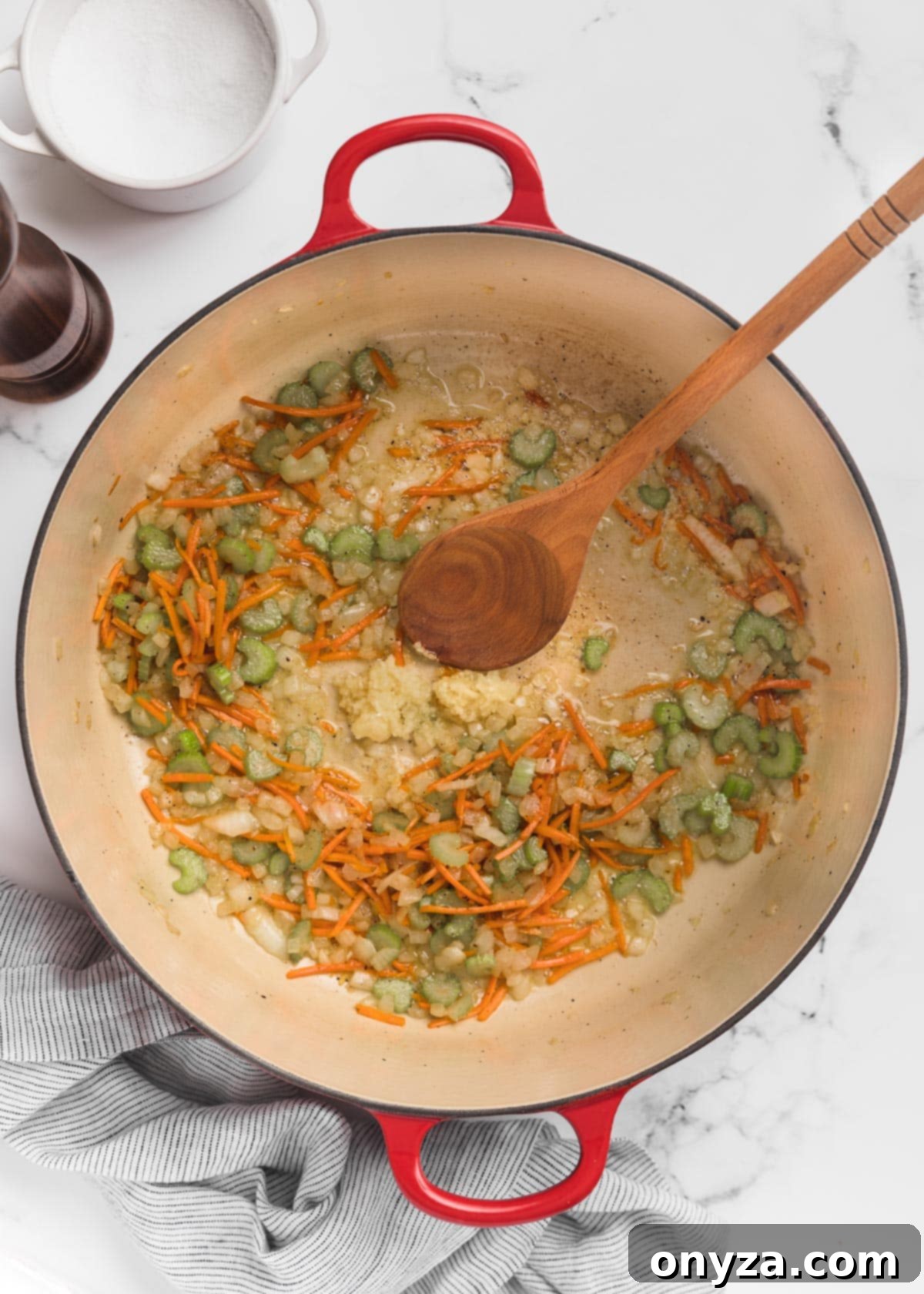 Hearty Chicken Gnocchi Comfort 5 sauteed mirepoix in a Dutch oven with a wooden spoon on a marble board