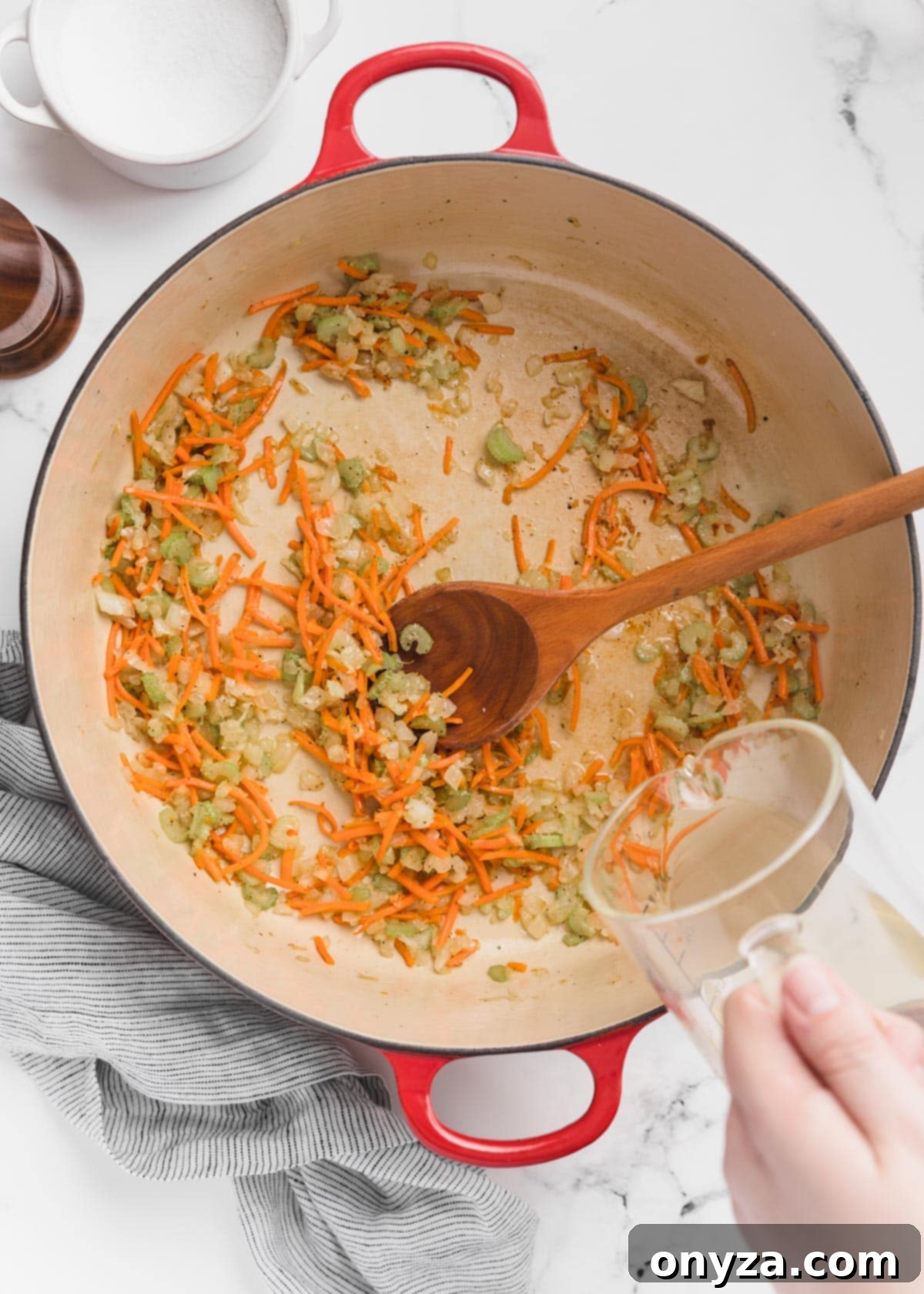 Hearty Chicken Gnocchi Comfort 6 white wine being poured from a glass measuring cup into a Dutch oven with sauteed mirepoix.