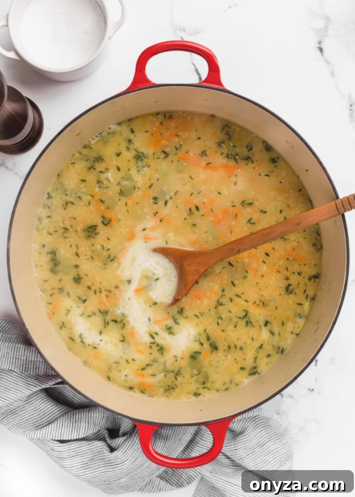 Hearty Chicken Gnocchi Comfort 8 chicken stock, half and half, and herbs added to a Dutch oven. A wooden spoon sits in the pot.